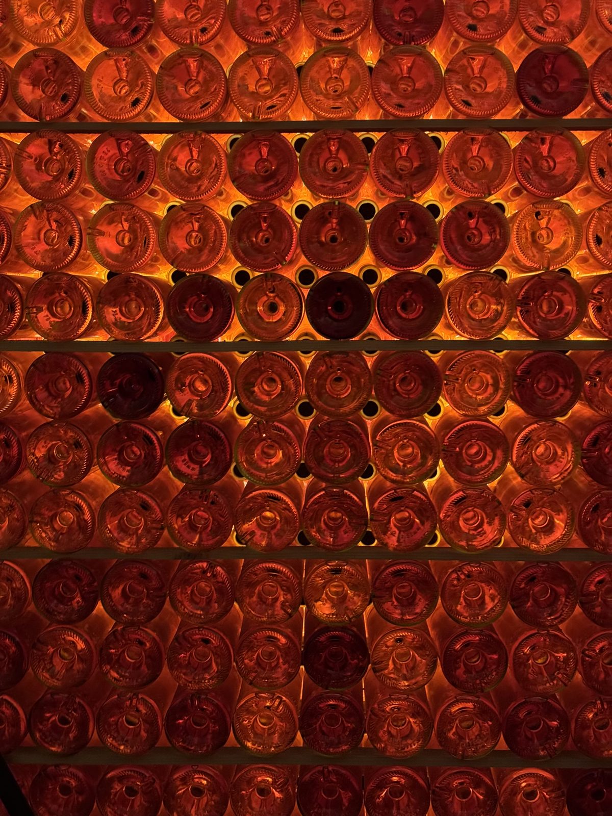 A wall of backlit bottles glowing orange and red