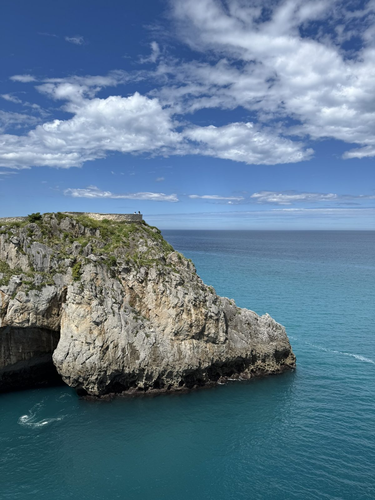 A rocky headland above turquoise sea under a cloudy blue sky