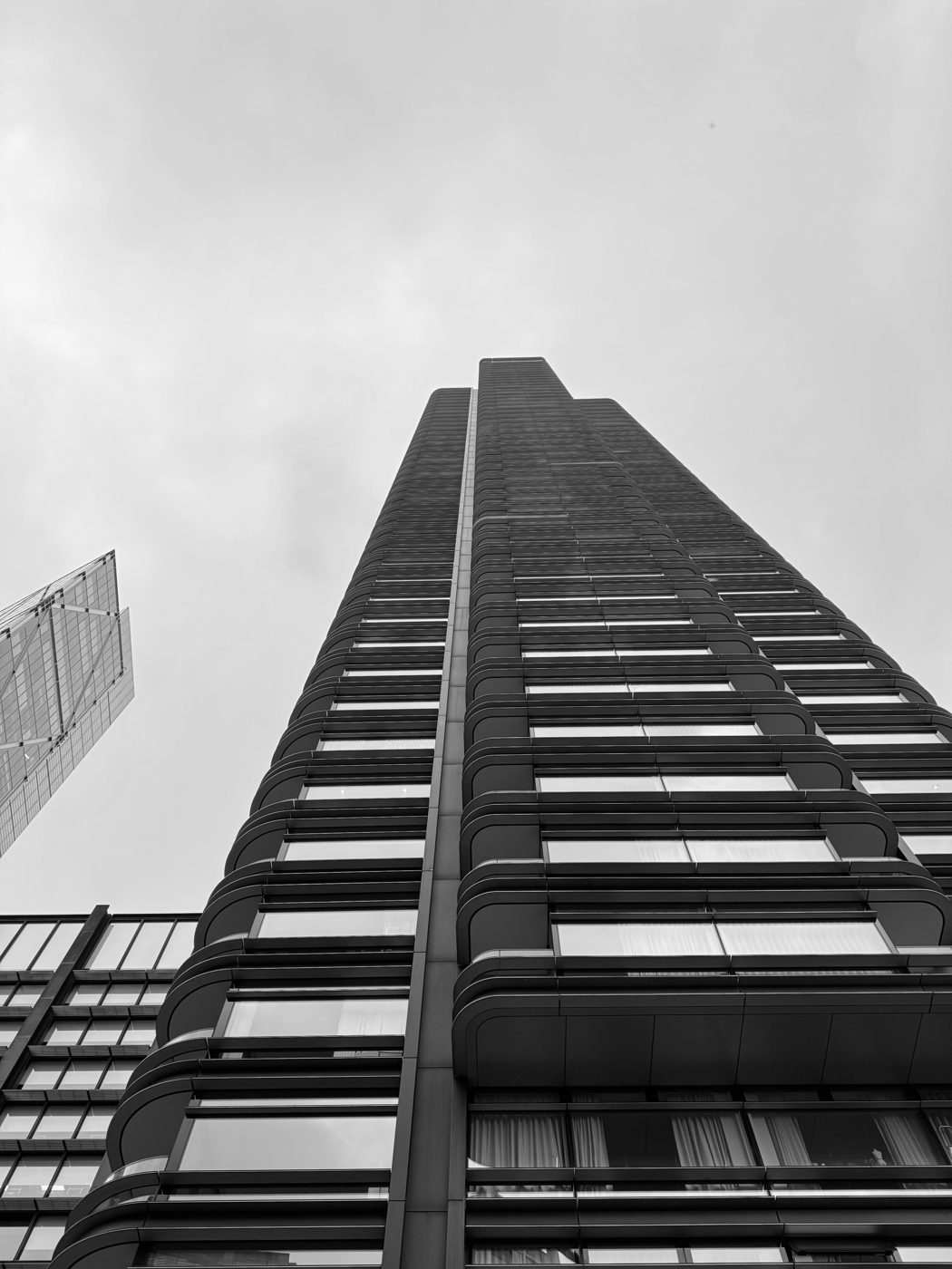 A residential tower shot from below, its balconies stacked like ruled lines