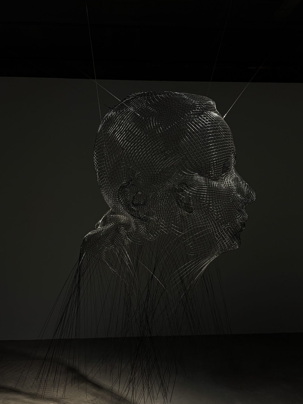 A sculpture of a head drawn in suspended wire, in a dark gallery