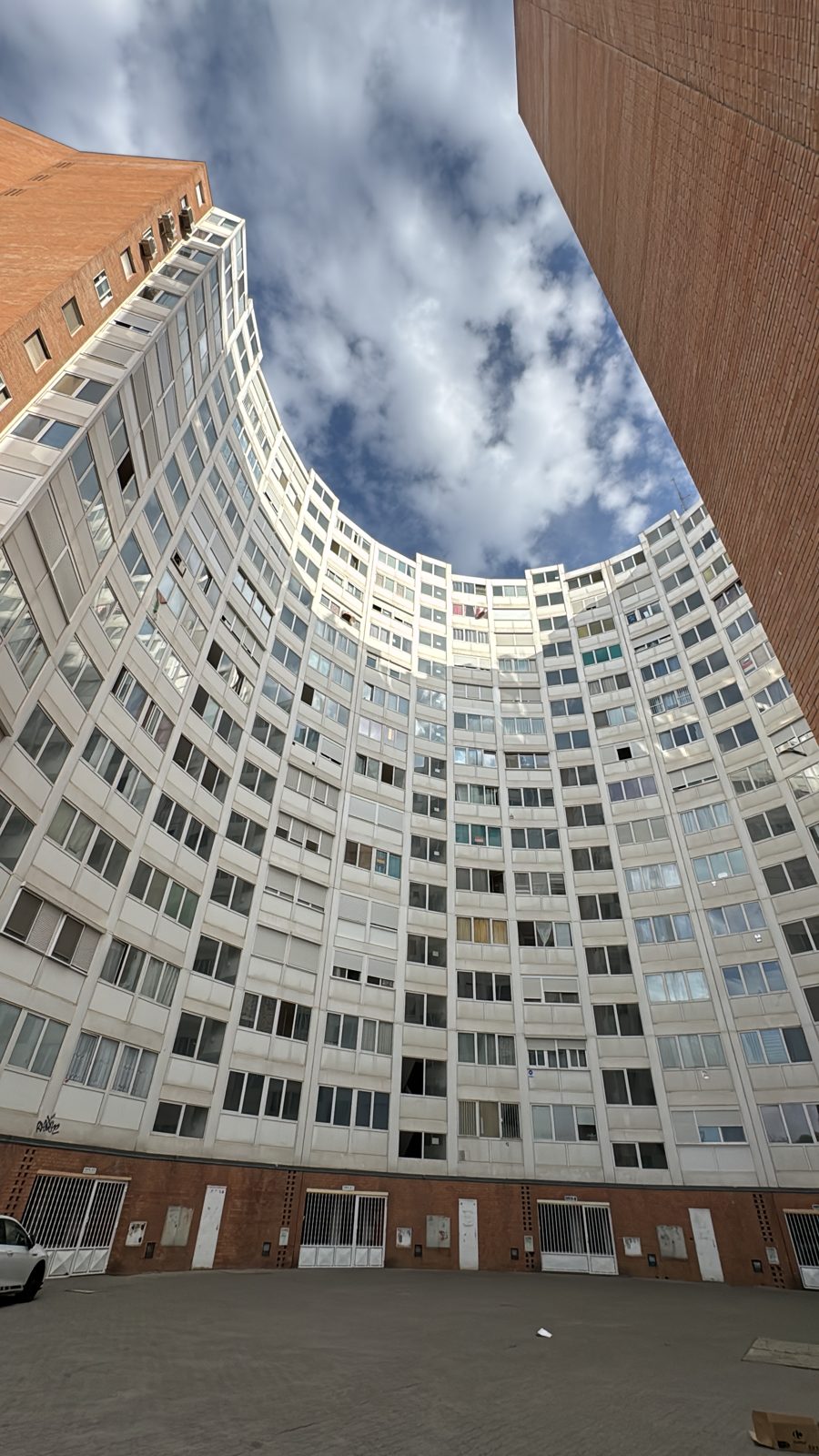 A curved residential block seen from its courtyard, looking up at the sky