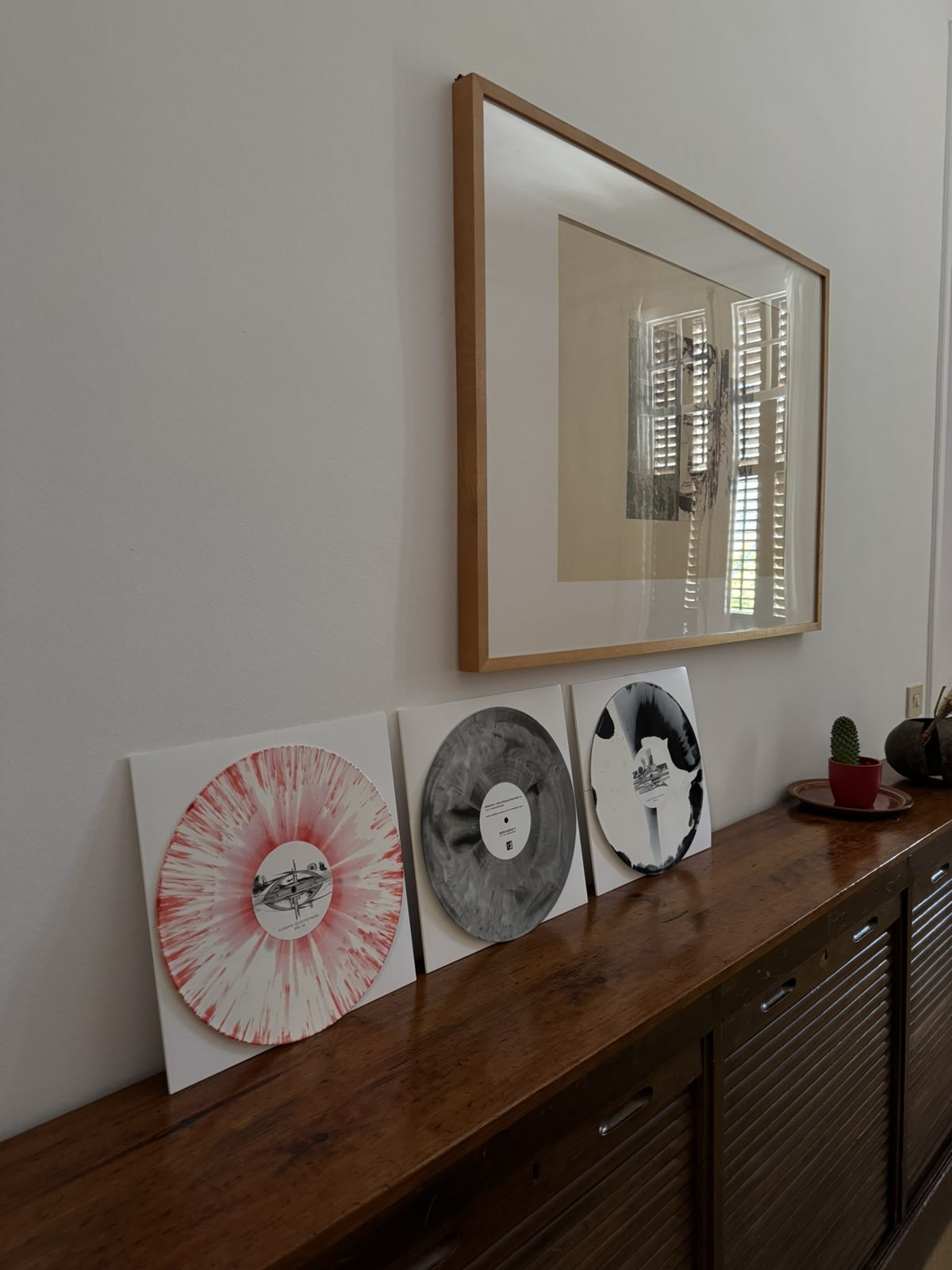 Three records leaning against a wall under a framed artwork