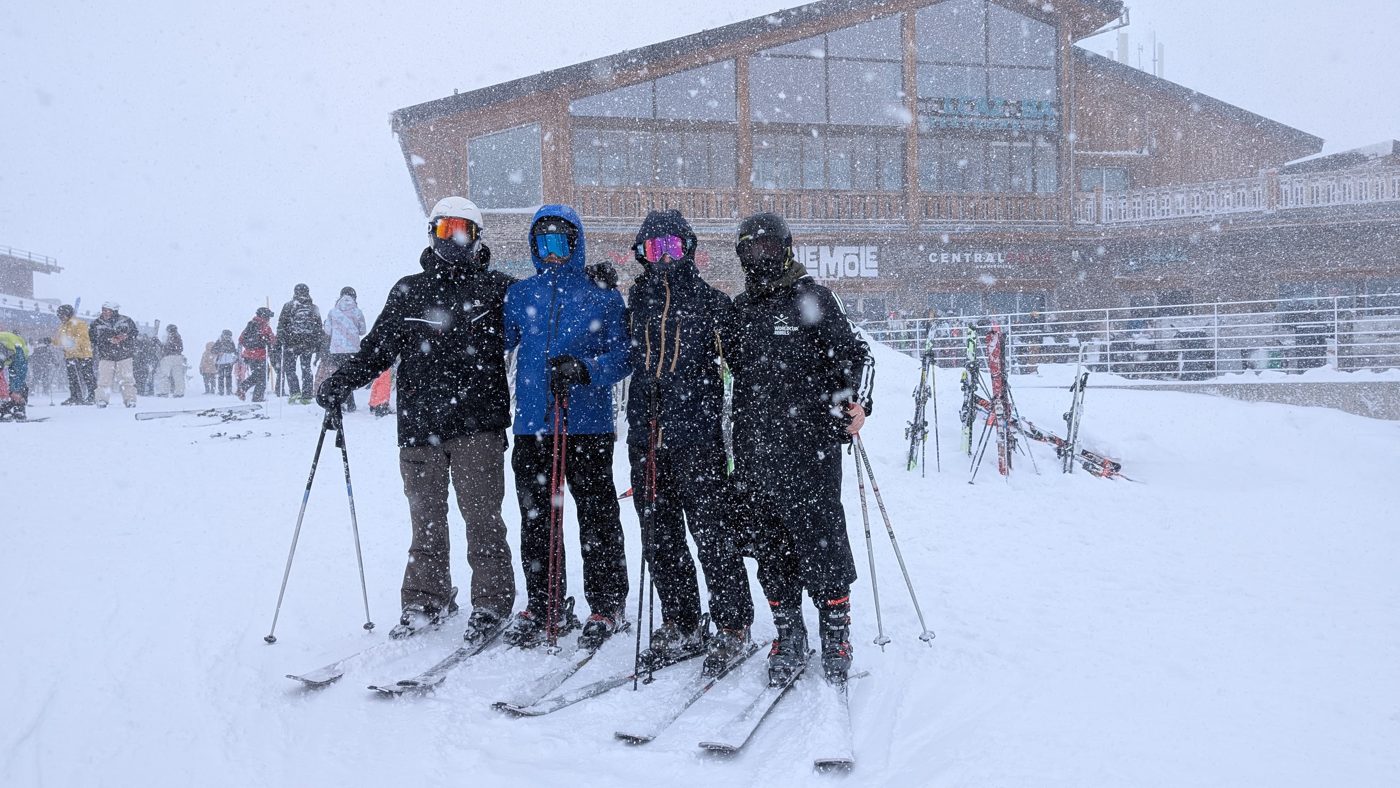 Four friends in ski gear in front of a mountain lodge