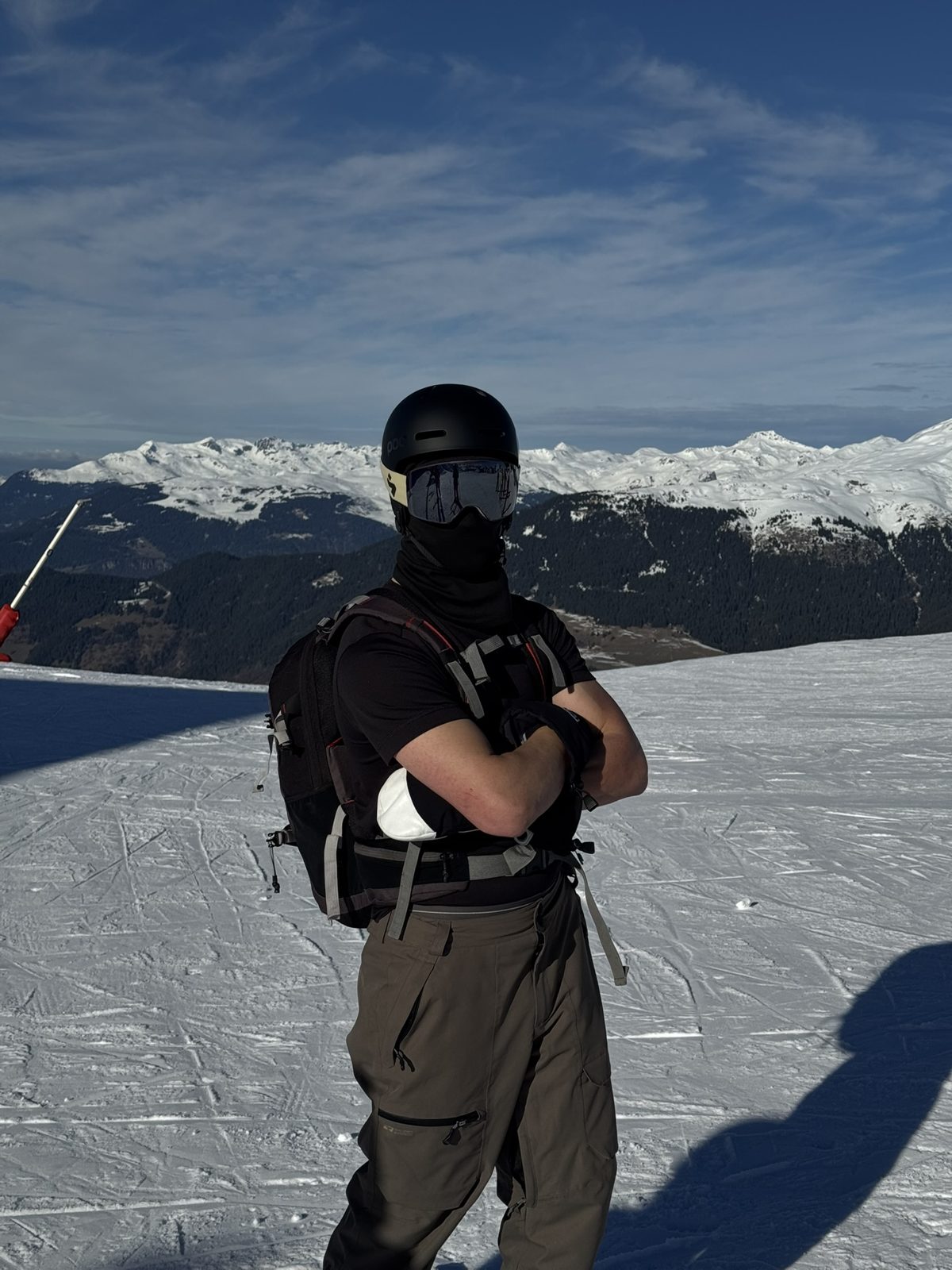 A skier in helmet and goggles standing on a groomed slope with snowy peaks behind