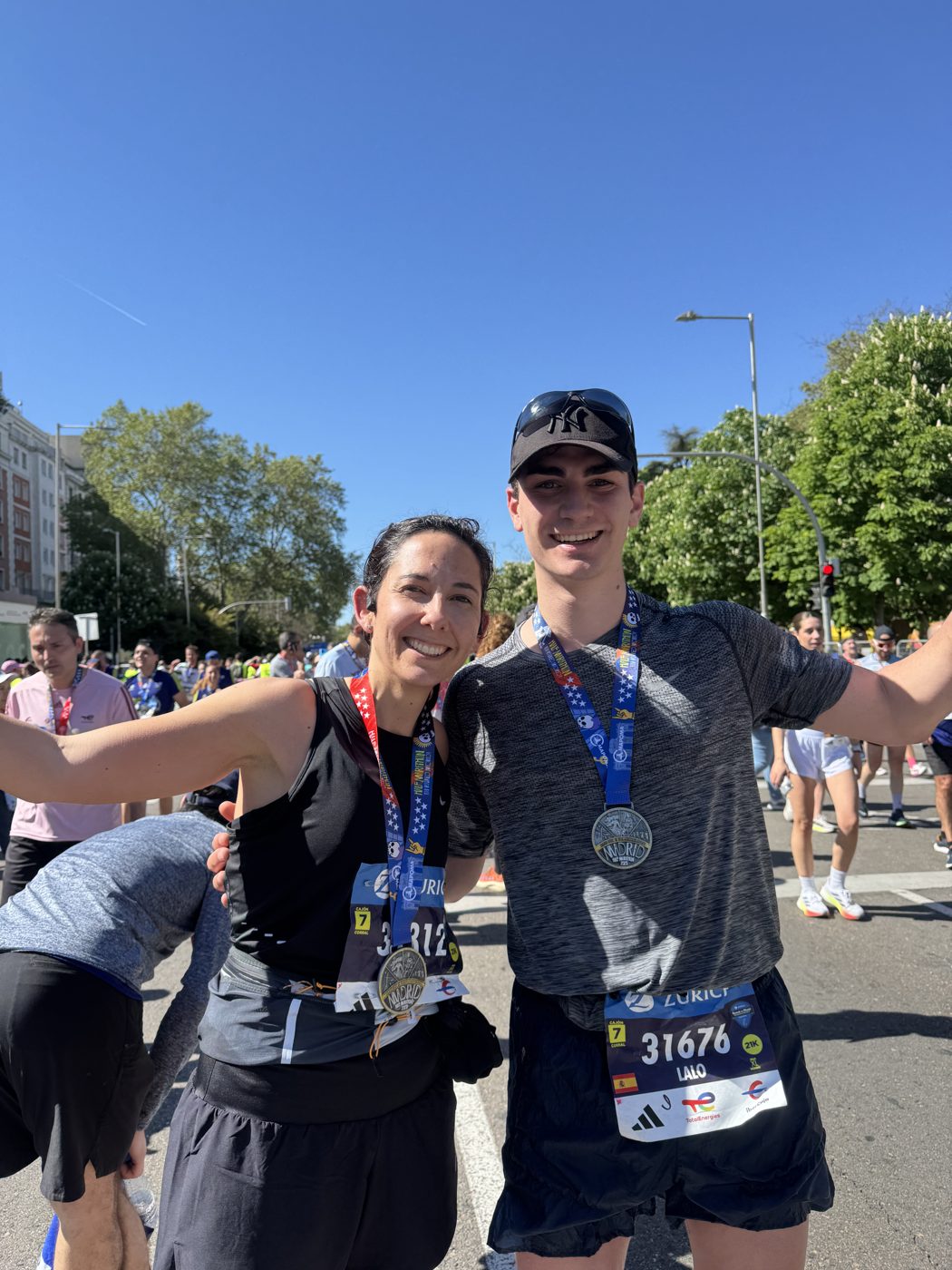 Two runners with finisher medals, smiling on a sunny city street